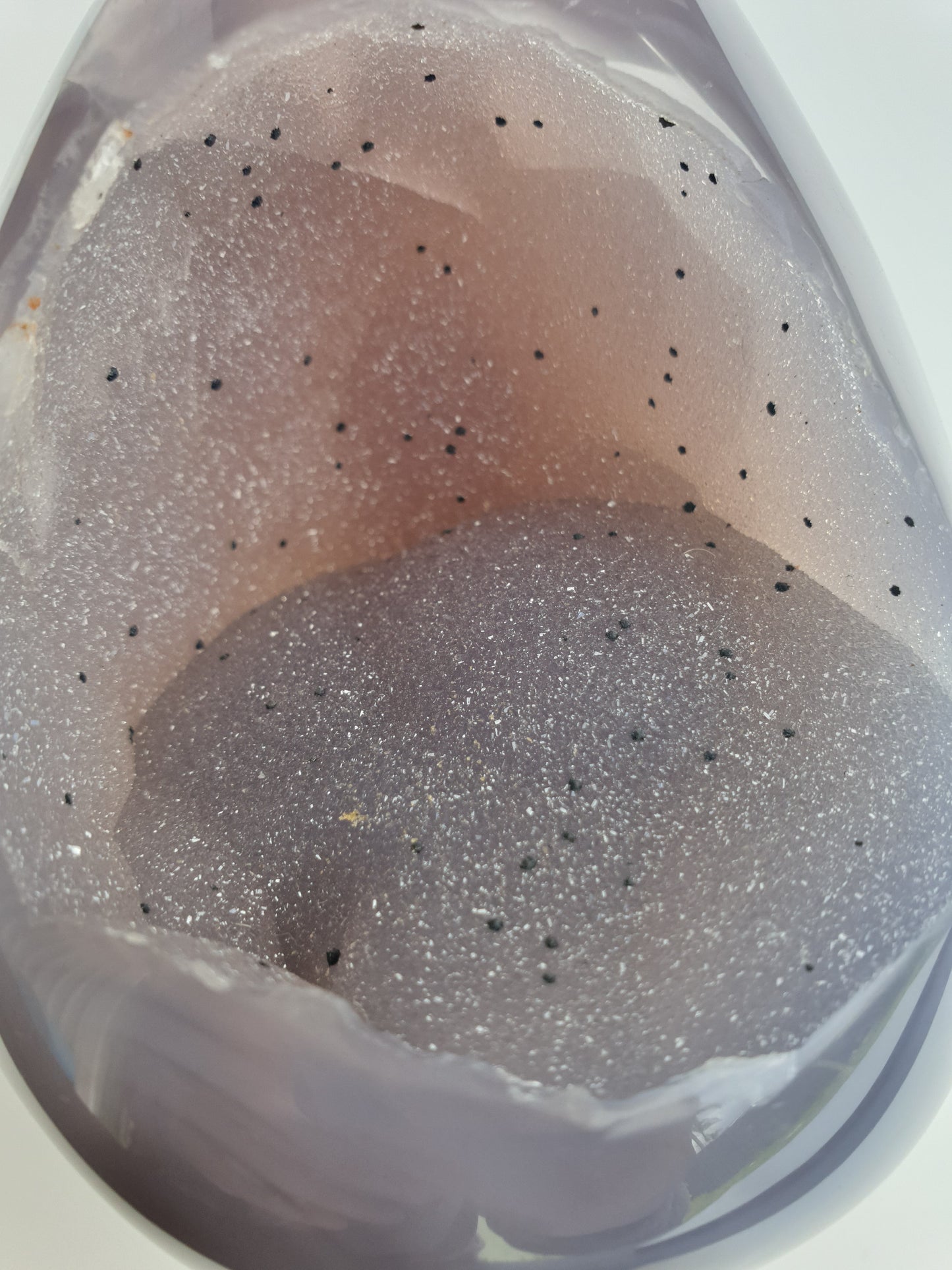 view of front of the agate egg. kiwi fruit looking - very sparkly, black spots throughout and has a gorgeous light peach / blue, grey colouring. outside is smooth, polished and has a light purple colour to it. very sparkly