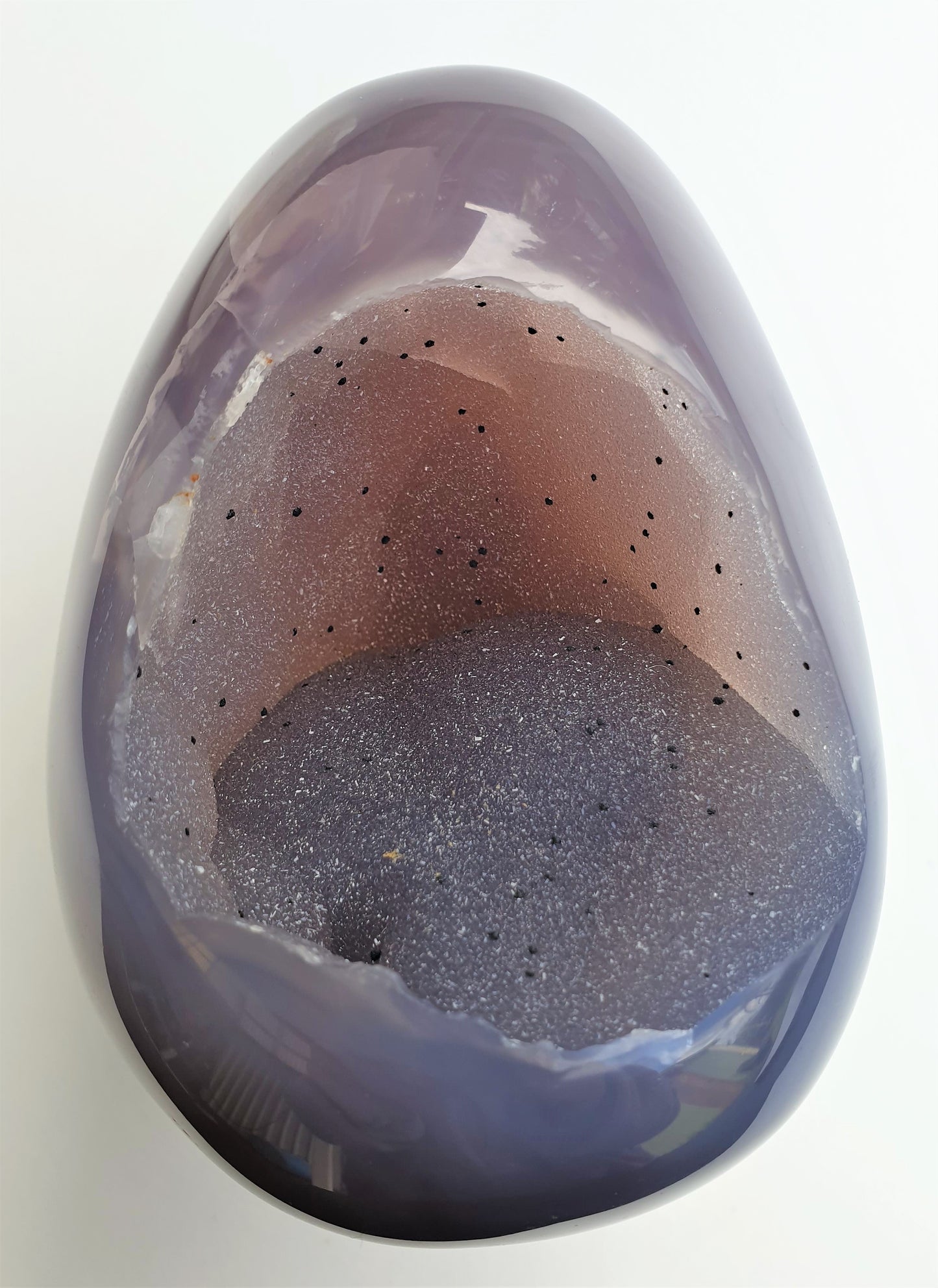 view of the whole agate egg druzy cave on the agate egg. kiwi fruit looking - very sparkly, black spots throughout and has a gorgeous light peach / blue, grey colouring. outside is smooth, polished and has a purple colour to it.